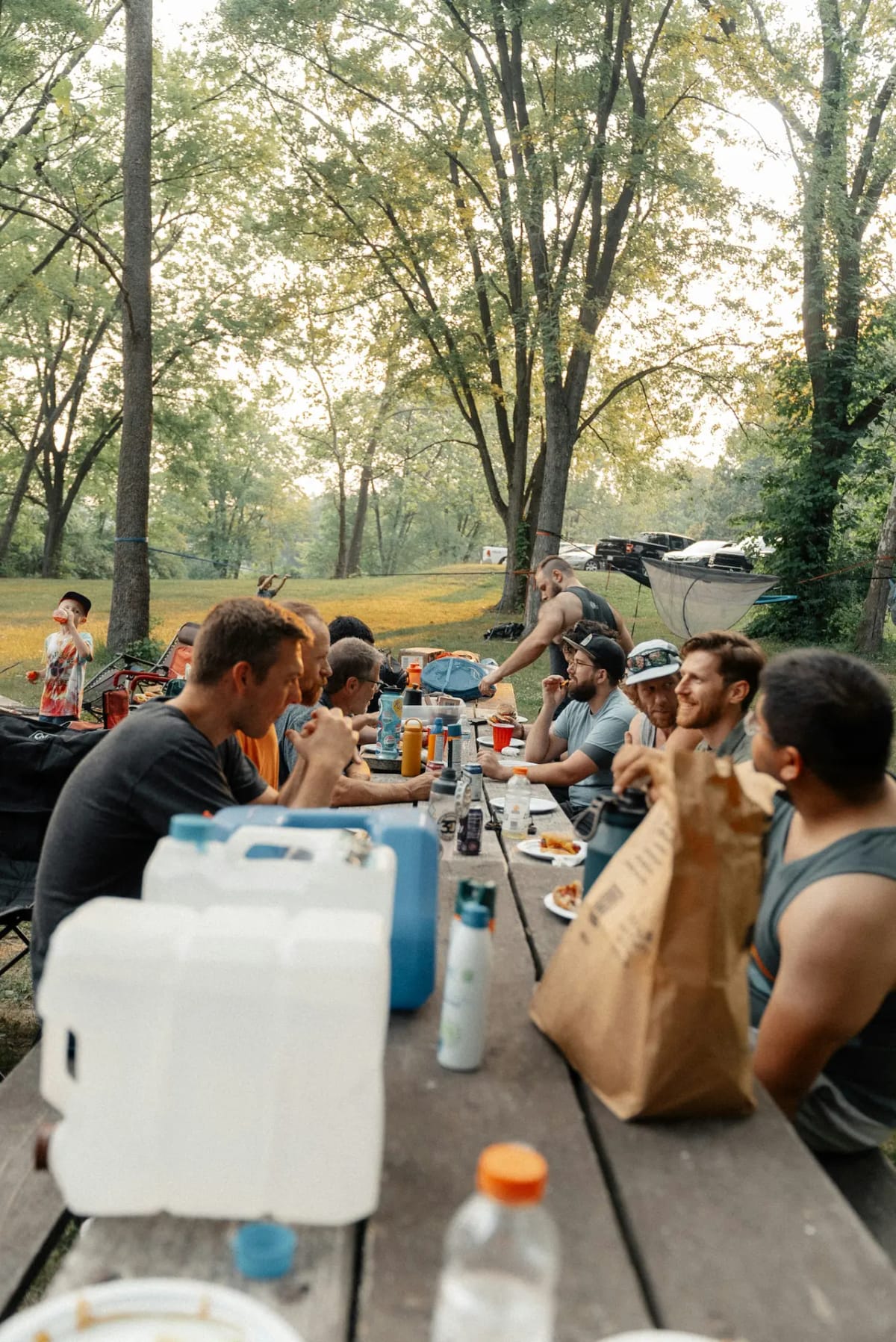 group of men sitting at a picnic table in a park with trees