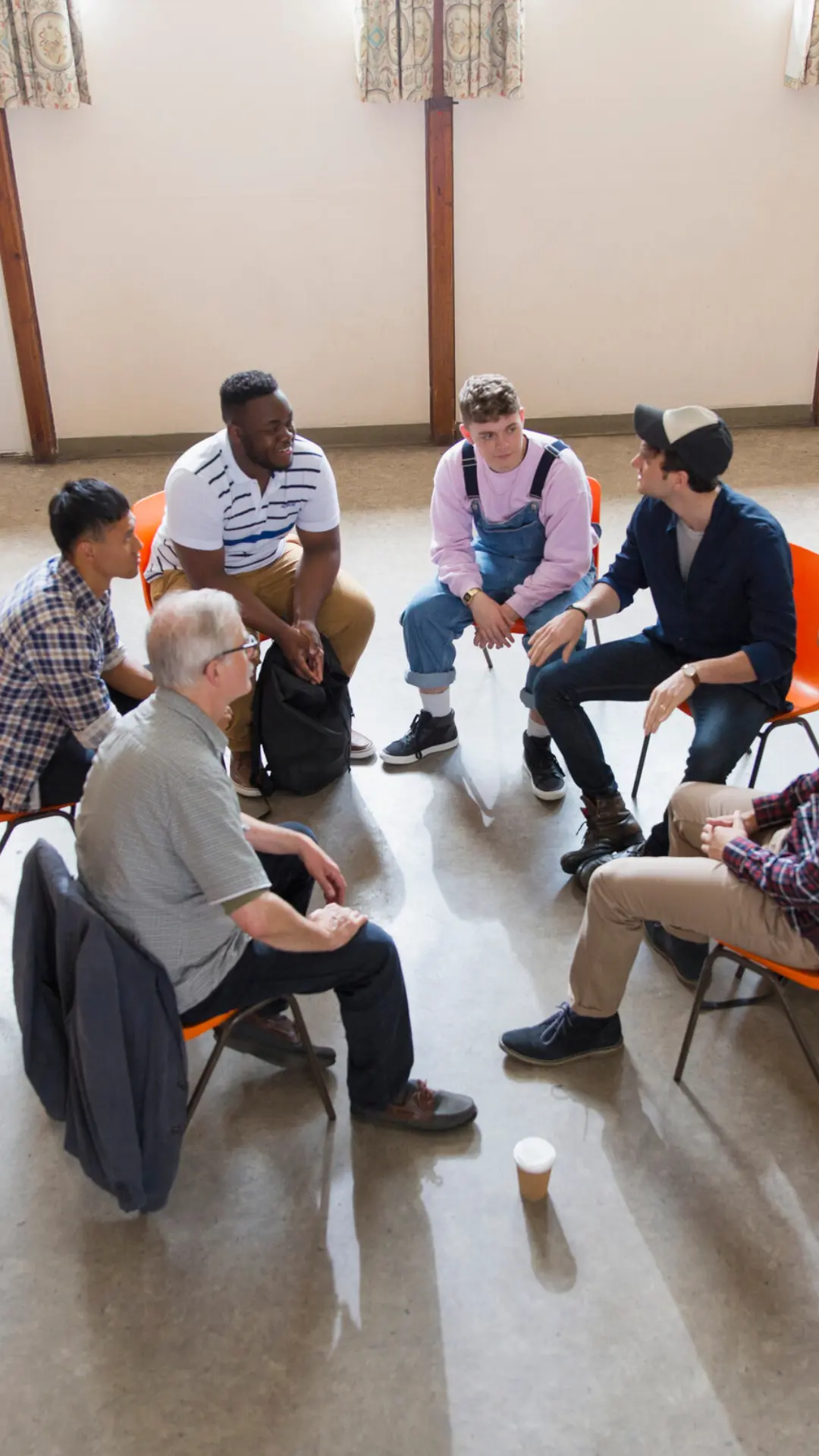 group of men sitting in orange chairs in a circle in a room
